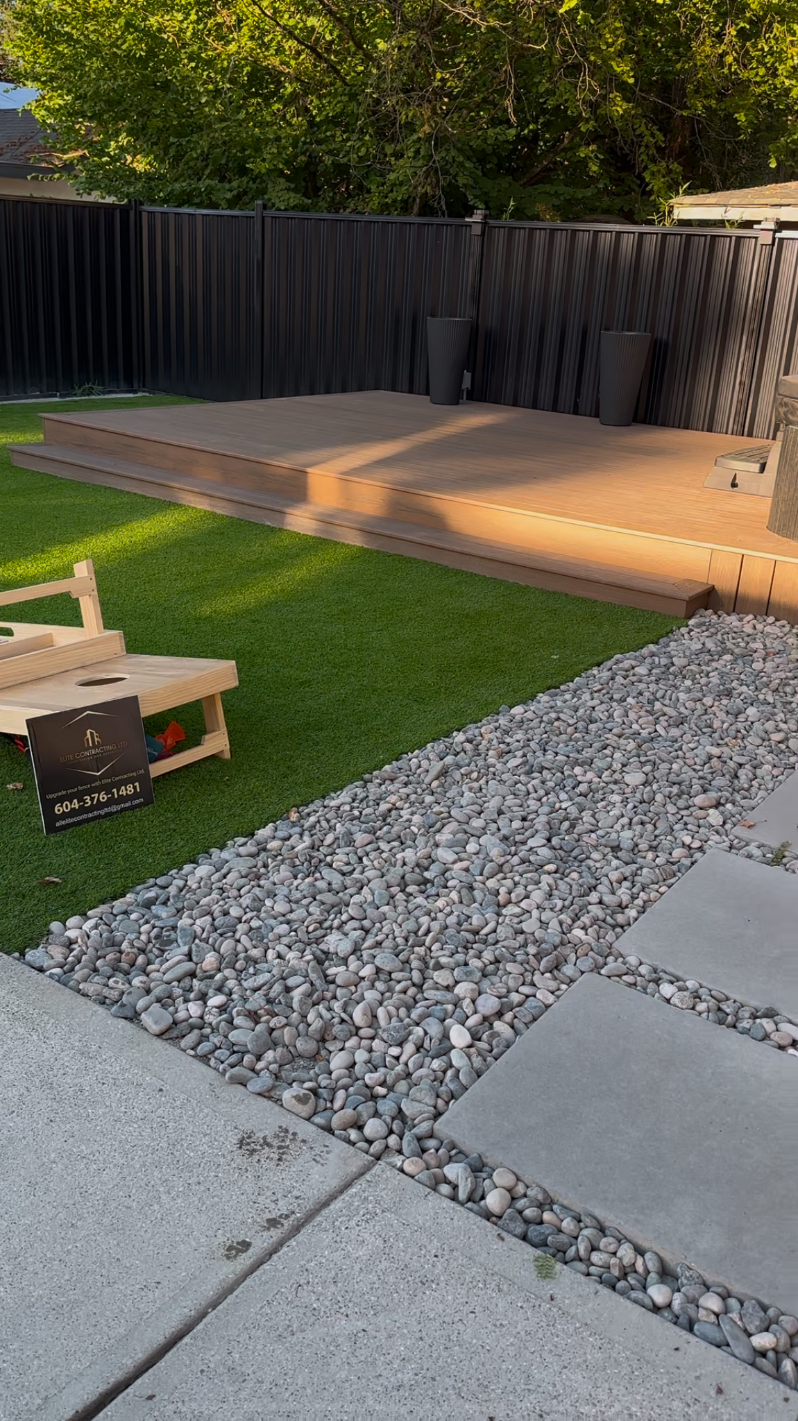 Completed backyard with artificial turf, composite deck and river rock border by Elite Contracting Ltd.