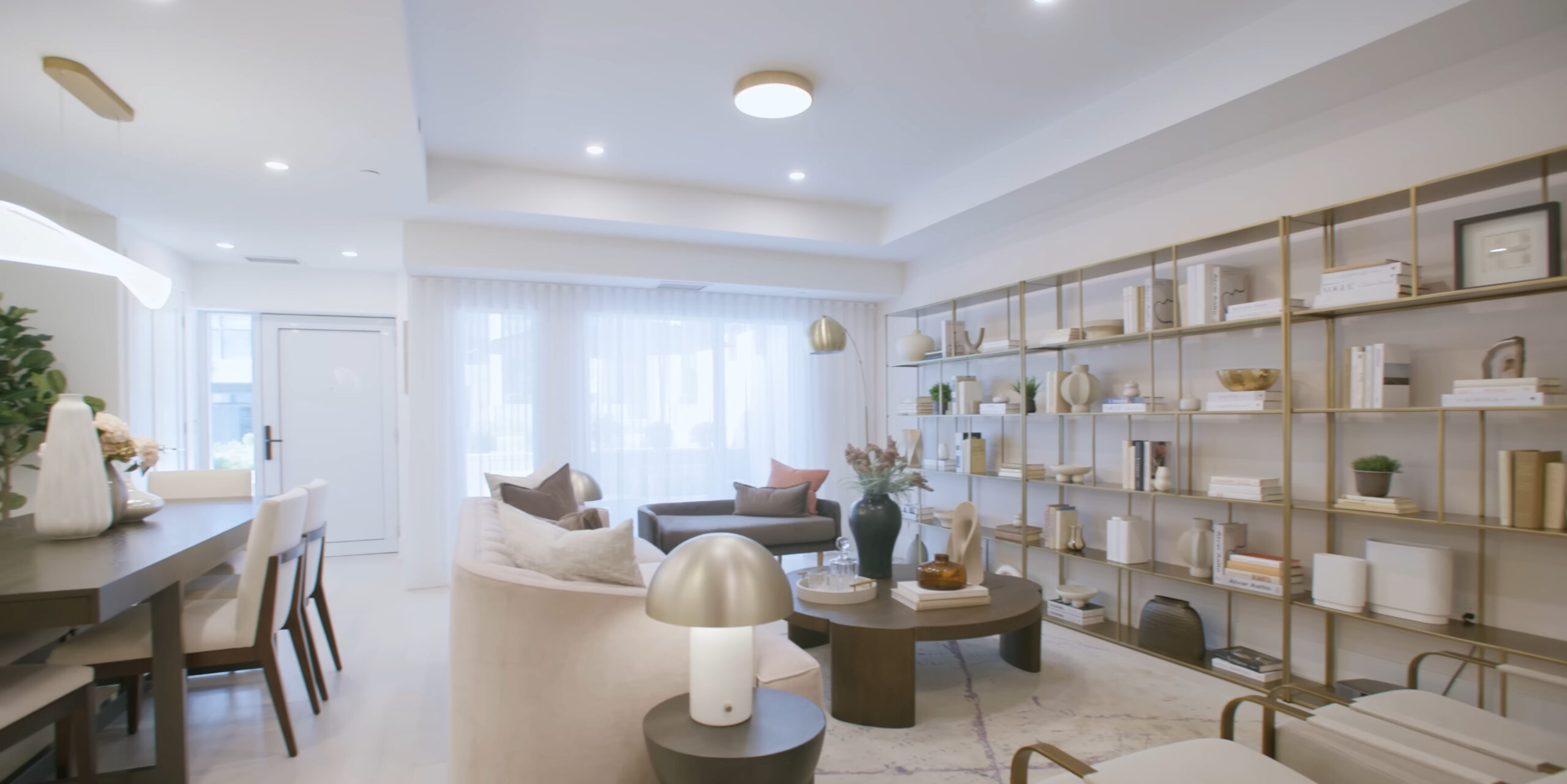 Renovated living and dining area with custom brass shelving and layered lighting