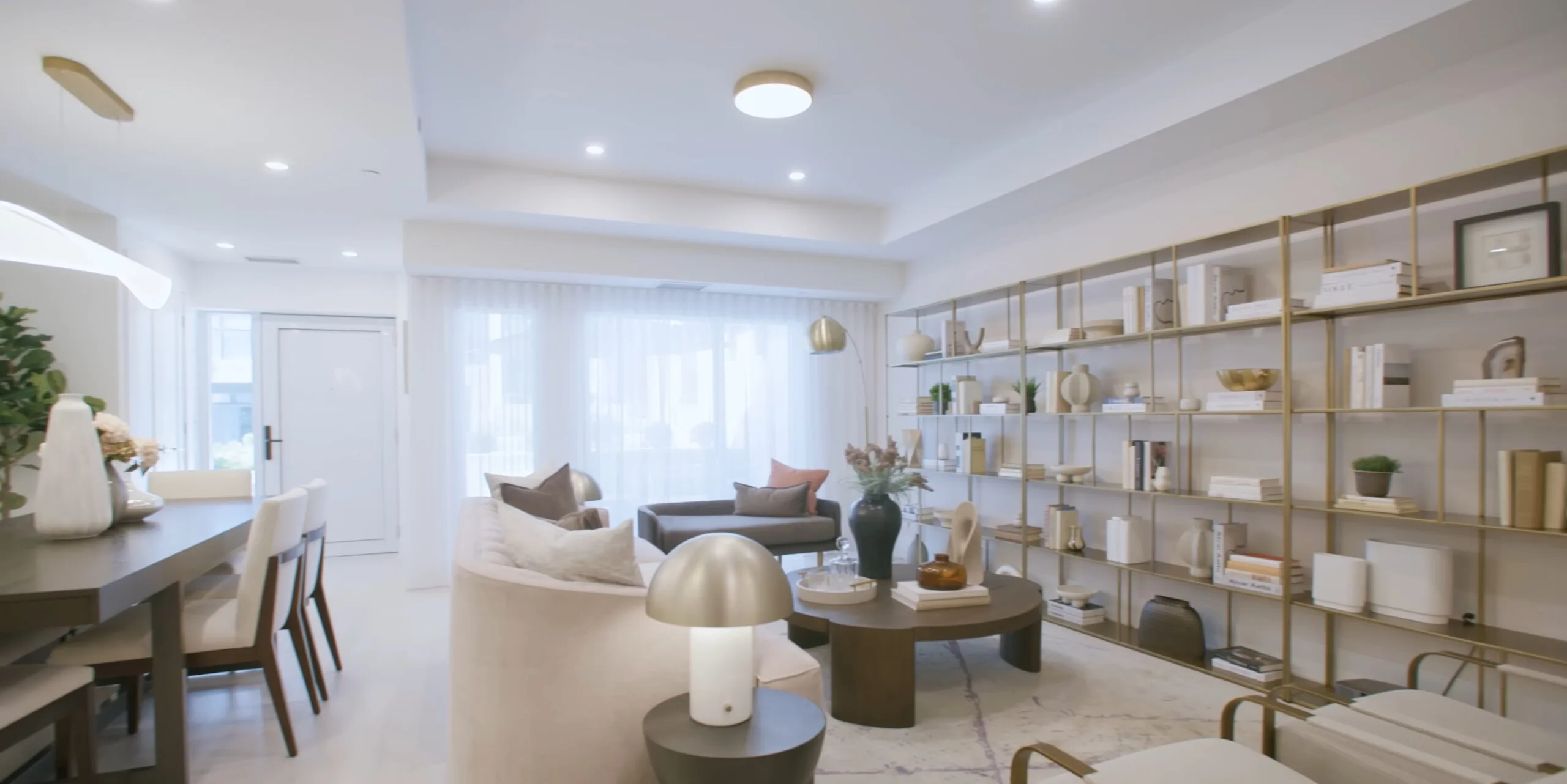 Renovated living and dining area with custom brass shelving and layered lighting