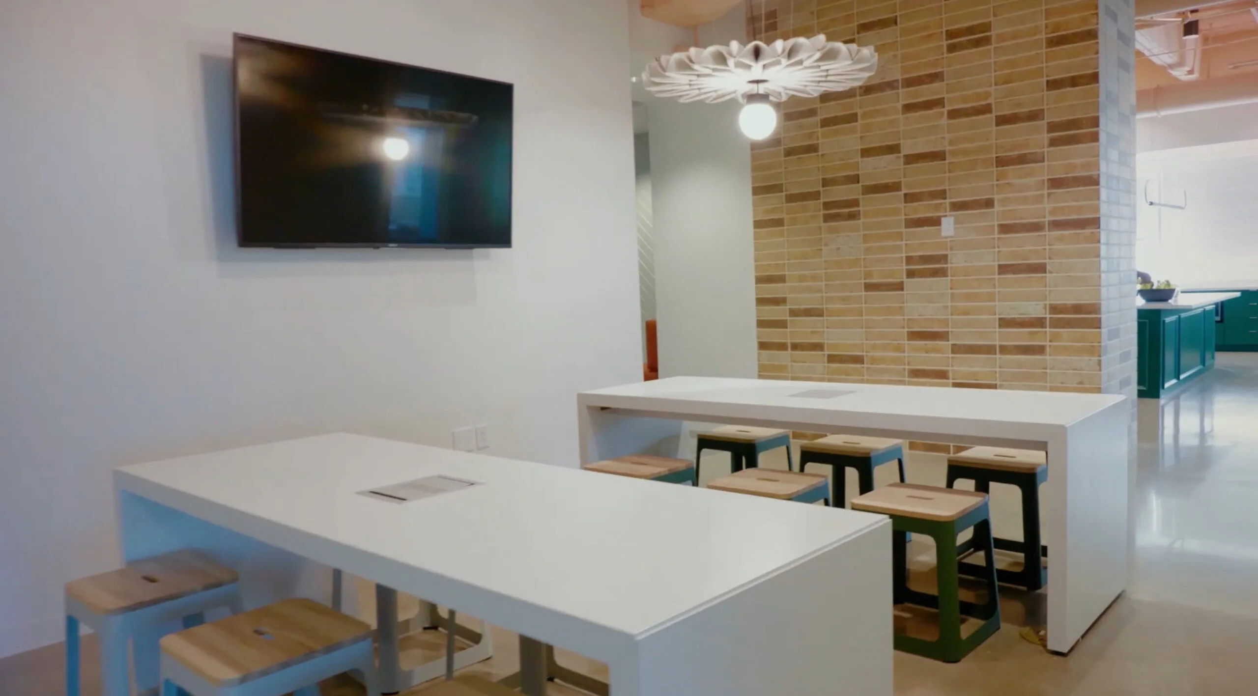 Commercial break area with communal tables, stools and a wall-mounted screen