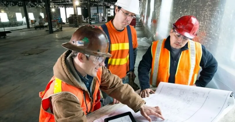 Construction workers in hard hats reviewing building plans on site
